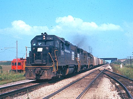 Penn Central 7847, leads a westbound train through Delta, Ohio on the main line going towards Elkhart and Chicago.  In the background, the Detroit, Toledo & Ironton crosses overhead.  The Wabash Railroad is to the right, out of the photo, and you can also observe an old interurban car to the left.  September, 1972  [Mark Dobronski]