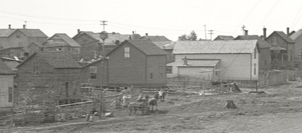 Here we have a view of the adjacent housing which is most likely owned by the mine itself. Some points of interest are; The martin house atop the electric pole.Many structures are on top of piers and do not have foundations. No cars just horses and buggies.  Every yard has a fence and types are varied.