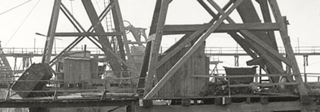 In this closeup view of the head frame, we can see one of the skips tipped up and what appears to be a wagon most likely for tailings.